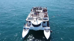 Un gran catamarán navega bajo el claro cielo azul de Valencia, lleno de gente disfrutando de un "Paseo en catamarán por Valencia". - ForTwo - Planes para parejas