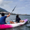 Dos personas en un kayak rosa disfrutan de la tranquilidad de las aguas de Getxo, dando un tranquilo "Paseo en kayak por Getxo" cerca de la ciudad costera bajo un cielo nublado. - ForTwo - Planes para parejas