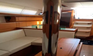 El interior de la cabina del barco cuenta con muebles de madera, asientos con cojines blancos y estantes de fondo, ideales para un relajante paseo en velero con vista de delfines. - ForTwo - Planes para parejas