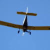 Un pequeño avión amarillo planea bajo un cielo azul claro, ofreciendo la experiencia "Piloto por un día en Atarfe" que captura la emoción de volar. - ForTwo - Planes para parejas
