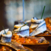 Primer plano de un plato de pescado elegantemente presentado con guarniciones y salsa, evocando una creación del famoso Taller de Pinchos de Bilbao, todo bellamente dispuesto en bandejas de madera para servir. - ForTwo - Planes para parejas