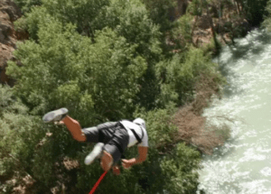 Un adicto a la adrenalina entra en acción con "Puenting en el río Genil", saltando en bungee sobre el hermoso río en medio de un dosel de árboles verdes para una aventura emocionante. - ForTwo - Planes para parejas