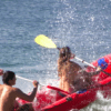 Dos aventureros practicando Rafting en el Río Mijares, navegando hábilmente entre las turbulentas olas mientras el agua salpica a su alrededor. - ForTwo - Planes para parejas