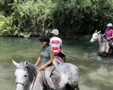 Los jinetes cruzan elegantemente el río poco profundo Valle del Río Ser, envuelto en una exuberante vegetación, en su aventura Ruta a Caballo por el Valle del Río Ser. - ForTwo - Planes para parejas