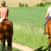 Dos personas disfrutan de una Ruta a caballo por Bilbao por un sendero a través de campos verdes bajo el cielo soleado. - ForTwo - Planes para parejas