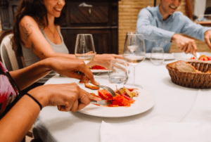Comensales saboreando tapas de la "Ruta de Tapas y Vinos en Valencia" con copas de vino rebosantes de vino y una cesta de pan, saboreando los vibrantes sabores que recuerdan a una velada valenciana. - ForTwo - Planes para parejas