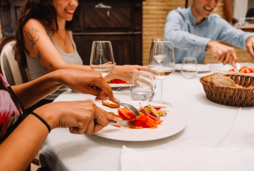 Comensales saboreando tapas de la "Ruta de Tapas y Vinos en Valencia" con copas de vino rebosantes de vino y una cesta de pan, saboreando los vibrantes sabores que recuerdan a una velada valenciana. - ForTwo - Planes para parejas
