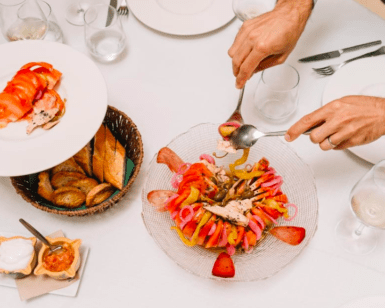 Una persona presenta la ruta de tapas y vinos de Valencia, acompañada de una cesta de pan y salsas, creando una animada escena gastronómica en la mesa. - ForTwo - Planes para parejas