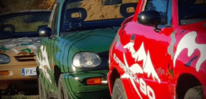 Tres autos estacionados, cada uno con diseños únicos (camuflaje, verde con barras y rojo con gráficos de montaña) están listos para una Ruta en 4x4 por Sierra Morena a través de los terrenos accidentados. - ForTwo - Planes para parejas