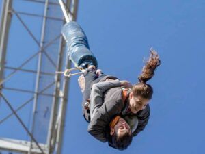 Dos personas disfrutan de un Salto Bungee Tándem en Lloret de Mar, colgando boca abajo contra un cielo azul claro. - ForTwo - Planes para parejas