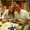 Dos personas sonríen mientras elaboran zapatos en una mesa de madera, inmersos en la atmósfera vibrante de un Taller de Alpargatas en Valencia. - ForTwo - Planes para parejas