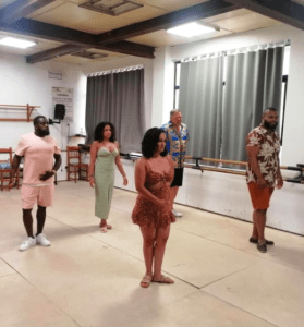 Cinco personas vestidas con ropa de verano brillante practican una rutina de baile en un estudio, que recuerda al Taller de Baile Latino de Valencia. - ForTwo - Planes para parejas