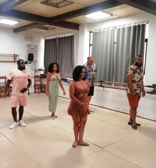 Cinco personas vestidas con ropa de verano brillante practican una rutina de baile en un estudio, que recuerda al Taller de Baile Latino de Valencia. - ForTwo - Planes para parejas