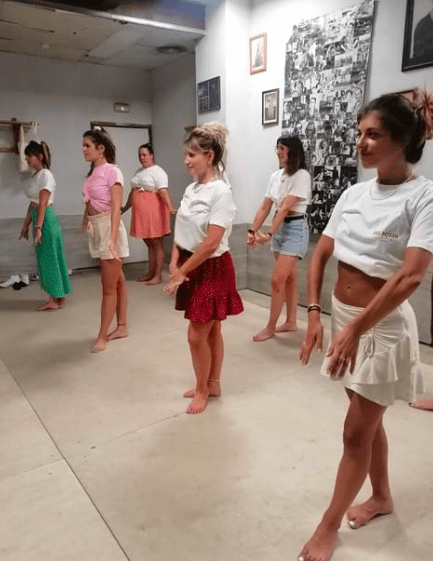 Durante una dinámica sesión del Taller de Baile Latino en Valencia, mujeres descalzas practican en el estudio, vestidas con faldas y blusas informales. Sus movimientos rítmicos reflejan la vibrante energía al deslizarse con gracia por la pista. - ForTwo - Planes para parejas