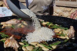 Arroz, pollo, judías verdes y ajo se añaden a una sartén grande como parte de la Experiencia Completa del Taller de Paella en Villa Indiano. - ForTwo - Planes para parejas