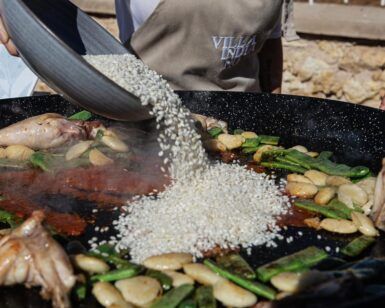 Arroz, pollo, judías verdes y ajo se añaden a una sartén grande como parte de la Experiencia Completa del Taller de Paella en Villa Indiano. - ForTwo - Planes para parejas