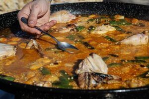 Un chef mezcla hábilmente una colorida paella llena de carnes y verduras en una sartén grande, capturando la esencia de la Experiencia Completa del Taller de Paella en Villa Indiano. - ForTwo - Planes para parejas