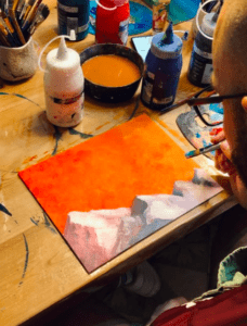 En Palma, un artista pasa las tardes en el Taller de Pintura Acrílica en Palma, utilizando hábilmente los pinceles para crear una vibrante escena de atardecer con pintura acrílica vívida sobre una mesa de madera. - ForTwo - Planes para parejas