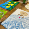 Las pinturas sobre una mesa de madera muestran limones, un diseño estampado y una figura con sombrero, con materiales de arte que hacen alusión al Taller de Pintura Acrílica en Palma. - ForTwo - Planes para parejas