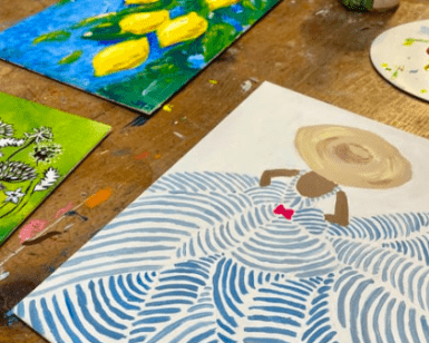 Las pinturas sobre una mesa de madera muestran limones, un diseño estampado y una figura con sombrero, con materiales de arte que hacen alusión al Taller de Pintura Acrílica en Palma. - ForTwo - Planes para parejas