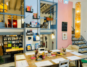 La pared con acento rosa y las luces colgantes del estudio de arte crean un ambiente animado para el Taller de Pintura Acrílica en Palma, con mesas preparadas para pintar y estantes llenos de suministros, ideales para darle vida al arte acrílico. - ForTwo - Planes para parejas