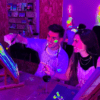 En una fiesta vibrante, dos personas pintan alegremente con colores neón bajo luz negra. La escena personifica el Taller de Pintura y Vino, donde el arte se fusiona con la celebración, y todos sonríen como si hubieran encontrado la combinación perfecta de creatividad y festividad. - ForTwo - Planes para parejas
