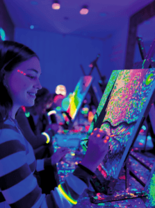En el vibrante Taller de Pintura y Vino, la gente crea obras de arte brillantes con colores neón bajo luz negra, combinando creatividad con magia luminiscente. - ForTwo - Planes para parejas