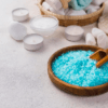 Un cuenco de madera de Taller Sales de baño mágico en Mallorca, rodeado de velas parpadeantes, piedras lisas y artículos de spa relajantes sobre una superficie clara, captura la esencia tranquila de Mallorca. - ForTwo - Planes para parejas