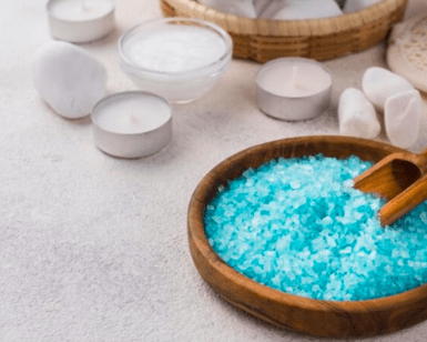Un cuenco de madera de Taller Sales de baño mágico en Mallorca, rodeado de velas parpadeantes, piedras lisas y artículos de spa relajantes sobre una superficie clara, captura la esencia tranquila de Mallorca. - ForTwo - Planes para parejas