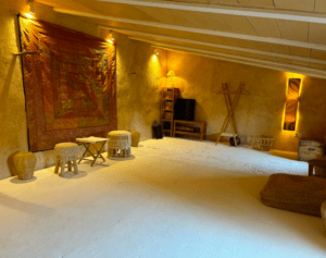 Habitación rústica cálidamente iluminada con taburetes de madera y un tapiz colorido que recuerda el encanto de Mallorca, que ofrece una acogedora zona de estar ideal para una escapada de Taller de Yoga Relajante en Mallorca. - ForTwo - Planes para parejas