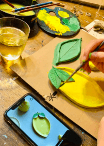 Una persona pinta hábilmente piezas de cerámica con forma de limón en vibrantes tonos verdes y amarillos, inspiradas en la imagen de Palma de un teléfono, durante el Taller de cerámica en Palma. - ForTwo - Planes para parejas
