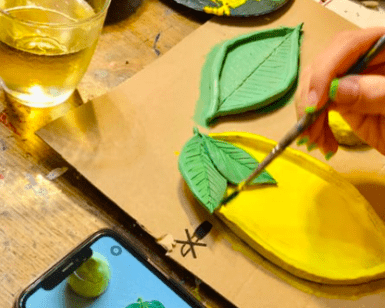 Una persona pinta hábilmente piezas de cerámica con forma de limón en vibrantes tonos verdes y amarillos, inspiradas en la imagen de Palma de un teléfono, durante el Taller de cerámica en Palma. - ForTwo - Planes para parejas