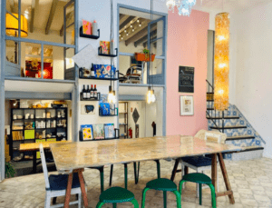 Una acogedora cafetería con una mesa de madera, sillas mixtas, paredes coloridas, exhibiciones de arte y una escalera adornada con azulejos con dibujos azules que recuerdan al Taller de cerámica en Palma. - ForTwo - Planes para parejas
