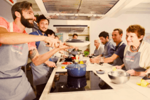 Los participantes disfrutan de una clase de cocina en grupo ambientada en una cocina moderna, saboreando los vibrantes sabores del Taller de cocina mediterránea en Mallorca, creando una excursión culinaria a Mallorca en su propio taller. - ForTwo - Planes para parejas