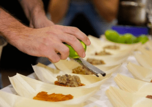 En el famoso Taller Mediterráneo de Sabores en Palma de Palma, una persona que ralla una lima realza diversos platos servidos en hojas de plátano, dando vida a sabores vibrantes. - ForTwo - Planes para parejas