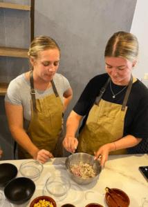 Dos personas con delantales mezclan ingredientes en un bol sobre la encimera de la cocina, recordando a una sesión de Taller Mediterráneo de Sabores en Palma. - ForTwo - Planes para parejas