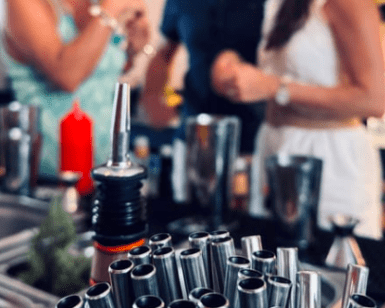 Una escena animada se desarrolla mientras la gente charla en un bar de Cala d’Or, con pajitas de cóctel en foco, evocando la esencia del Taller de coctelería en Cala d’Or. - ForTwo - Planes para parejas