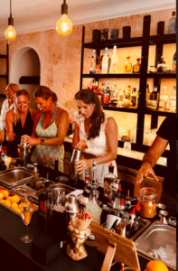 Los invitados se deleitan en un Taller de coctelería en Cala d’Or, rodeado de botellas y copas elegantemente dispuestas. - ForTwo - Planes para parejas