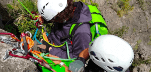 Dos escaladores con cascos y equipo ajustan cuerdas de colores en un acantilado rocoso, embarcándose en la emocionante aventura de la Vía Ferrata de Iniciación en La Cantera. - ForTwo - Planes para parejas