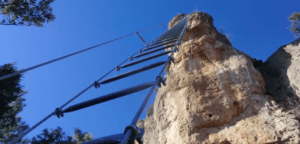 Una empinada escalera de metal escala un acantilado rocoso bajo un cielo azul claro, señalando el inicio de la Vía Ferrata de Iniciación en La Cantera. - ForTwo - Planes para parejas