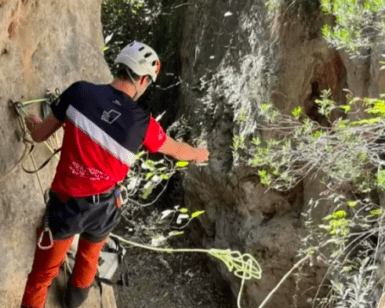 Equipado con material de seguridad, un escalador se enfrenta al terreno rocoso de La Cantera, agarrado a una cuerda en un estrecho paso del acantilado durante una emocionante experiencia en la Vía Ferrata de Iniciación en La Cantera. - ForTwo - Planes para parejas