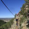 Una persona navega por la Vía Ferrata en Fuente de Godalla - Valencia con un arnés de seguridad bajo un cielo azul claro, encarnando la aventura. - ForTwo - Planes para parejas