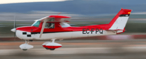 Un pequeño avión rojo y blanco despega con un desenfoque de movimiento dinámico, evocando la emoción de un vuelo en avión por Granada sobre sus paisajes escénicos. - ForTwo - Planes para parejas