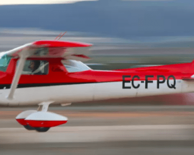 Un pequeño avión rojo y blanco despega con un desenfoque de movimiento dinámico, evocando la emoción de un vuelo en avión por Granada sobre sus paisajes escénicos. - ForTwo - Planes para parejas