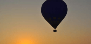 Una silueta de globo aerostático contra un cielo naranja del atardecer evoca la tranquilidad de un "Vuelo en globo en Valencia" sobre paisajes impresionantes. - ForTwo - Planes para parejas