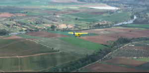 Una avioneta amarilla sobrevuela campos verdes y marrones, con el Pantano de Orellana brillando cerca, junto a un río serpenteante. Producto: Vuelo sobre el Pantano de Orellana. - ForTwo - Planes para parejas
