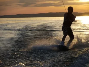 Una persona practica hábilmente el Wakeboard en Gandía sobre las brillantes aguas al atardecer, entre salpicaduras y un vibrante fondo naranja. - ForTwo - Planes para parejas