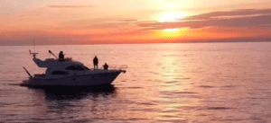 El Yate de lujo en Alcocéber navega por las serenas aguas, su forma resaltada contra una vívida puesta de sol y un cielo naranja. - ForTwo - Planes para parejas