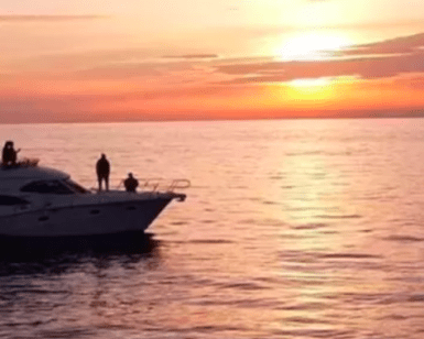 El Yate de lujo en Alcocéber navega por las serenas aguas, su forma resaltada contra una vívida puesta de sol y un cielo naranja. - ForTwo - Planes para parejas