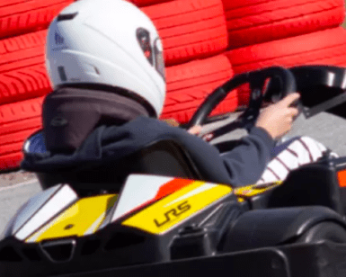 Un individuo con casco conduce un kart en una pista con barreras de neumáticos rojas y blancas, reflejando la emoción de los circuitos de karting en Empuriabrava. - ForTwo - Planes para parejas